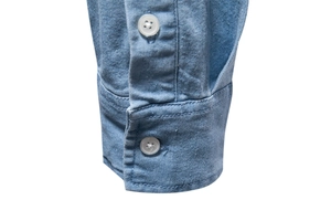 Close-up of light blue denim shirt cuff with white resin buttons and neat stitching