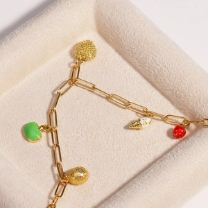 Detailed shot of a gold charm bracelet with enamel fruits in a beige jewelry tray