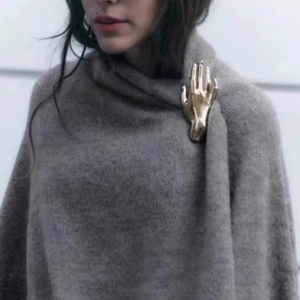 Golden polished metal hand-shaped brooch pinned on a grey knitted shawl for elegant styling