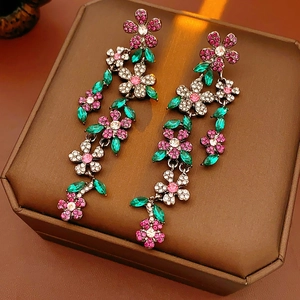 Détail de boucles d'oreilles fleurs à pompons avec strass roses et verts sur un coffret