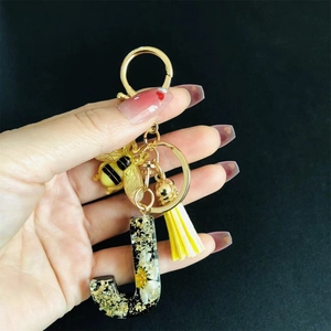 Detailed close-up of resin letter J keychain with real dried flowers, bee charm and yellow tassel