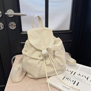 Detail of cream white nylon backpack featuring drawstring closure and white plastic buckle