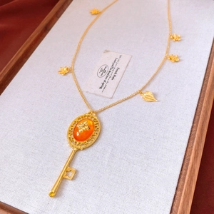 Detail of vintage gold key necklace with orange resin gemstone and leaf charms