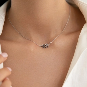 Close-up of a silver leaf pendant necklace on a woman wearing a white shirt
