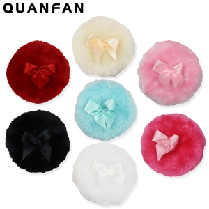 Close-up of colorful plush baby powder puffs with decorative ribbon bows on white surface