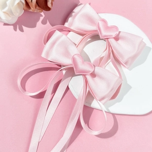Close-up of pink satin bow hair clips with heart charms on white display surface