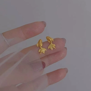 Detailed view of golden goldfish stud earrings held with elegant white translucent veil