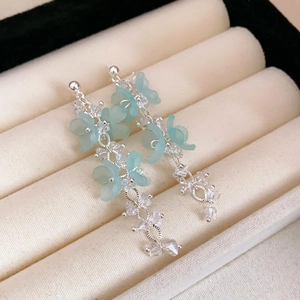 Gros plan de boucles d'oreilles fleurs bleu clair avec chaînes argentées sur boîte beige