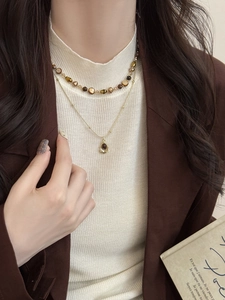 Détail d'un collier vintage à deux rangs en œil de tigre sur un pull en maille beige