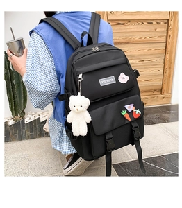 Detail of black canvas backpack featuring a plush bear pendant and cute cartoon patches