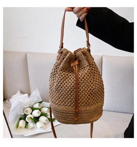 Detail of hand-woven straw bucket bag with brown leather strap and drawstring closure