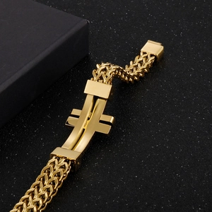 Macro shot of gold-plated stainless steel chain bracelet with polished cross charm on black