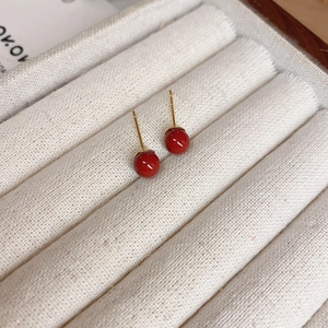 Macro shot of minimalist red bead stud earrings with gold-plated silver needles in box