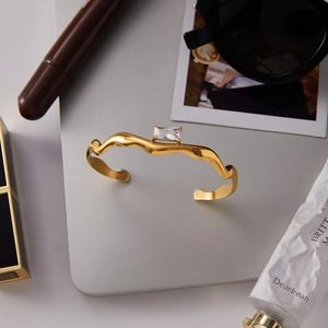 Gold-tone wavy open bangle with rectangular zircon on tablet surface lifestyle setup