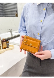 Detail of yellow mini leather pouch with snap closure and metal ring held by a model
