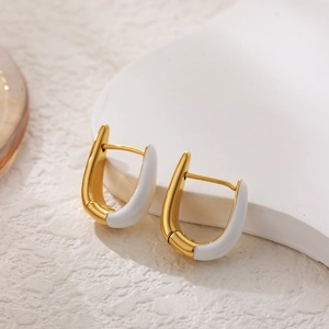 Macro detail of U-shaped gold earrings with white enamel finish on a textured background
