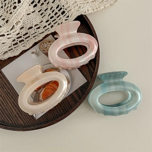 Three gradient marble oval hair claws in pink beige and teal displayed on wood