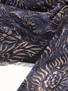 Détail du tissu en maille violet foncé avec des motifs de plumes dorées sur la jupe
