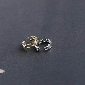 Close-up of gold and silver hollowed heart-shaped ear cuffs on a dark grey background