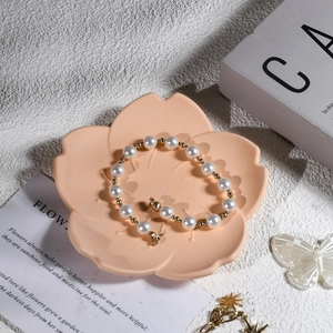 Perlenarmband mit Goldperlen und Bärenanhänger auf einer blumenförmigen Ablage