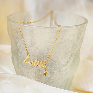 Detailed shot of golden Lolita name necklace with a green gemstone on frosted glass