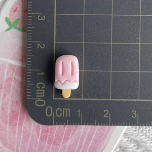 Close-up of a mini pink resin popsicle charm measured at 1.5cm on a scale mat