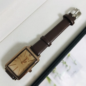 Detailed top view of a rectangular gold-tone watch with a brown leather strap in a gift box