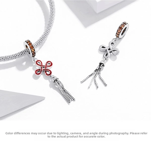 Close-up of Chinese knot charms with red enamel and tassels on a silver bracelet