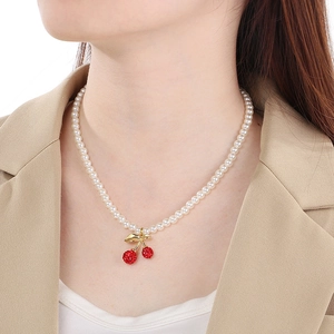 Elegant pearl necklace with red resin cherries and rhinestone pendant worn on a model