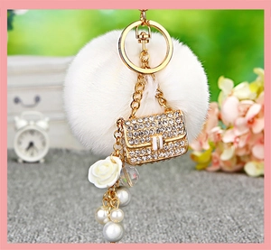 Detail of a white faux fur pompom keychain with a sparkling rhinestone gold mini bag charm