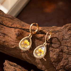 Macro detail of teardrop earrings with yellow dried flowers in gold textured metal frames