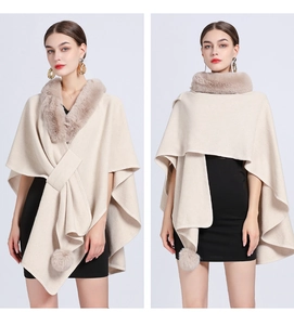 Detail of beige knit poncho with faux fur collar and decorative pom-poms on the front