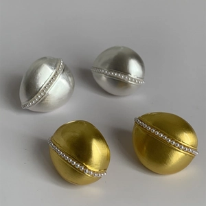 Dettaglio di orecchini ovali opachi oro e argento con eleganti perle incastonate