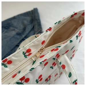 Close-up detail of smooth white fabric bag with red cherry print and golden zipper