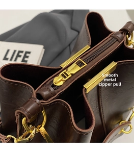 Detail of premium brown leather bucket bag with smooth gold zipper and sturdy metal D-rings