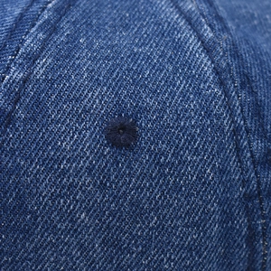 Detailed macro view of dark denim fabric texture and stitched eyelet on baseball cap