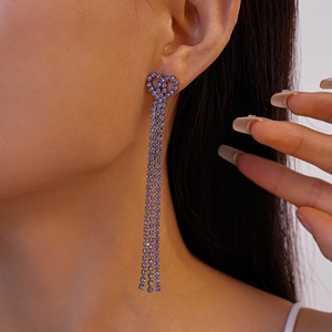 Macro view of model wearing purple rhinestone tassel earrings with a double heart stud