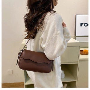 Detail view of a dark brown shoulder bag with wavy flap design on a white knit sweater