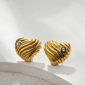 Macro detail of gold-plated heart stud earrings with ripple texture and zircon accent