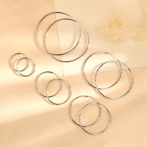 Set of five polished silver hoop earrings in assorted sizes displayed on a warm beige background
