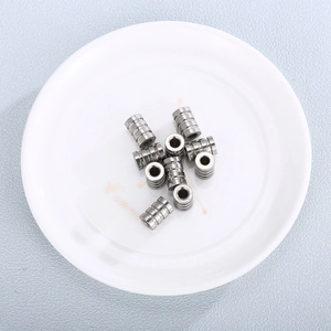 Grooved stainless steel cylindrical beads in a white dish for jewelry hardware making