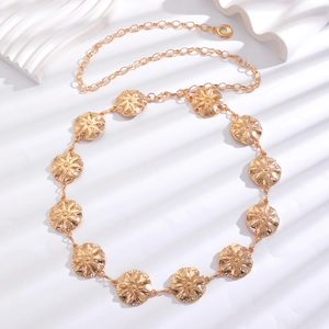 Detailed close-up of golden metal chain belt with sunburst textured floral medallions