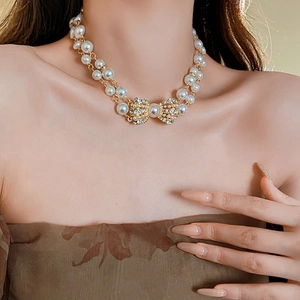 Close-up of a double-layer pearl necklace featuring a golden rhinestone bow pendant