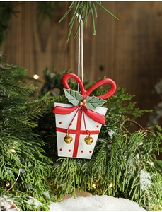 Detail of metal Christmas gift box ornament with holly leaves hanging on snowy pine branch