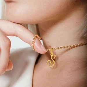 Detail view of a golden artistic letter S pendant on a classic ball chain necklace