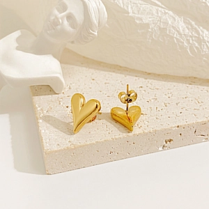 Close-up of heart stud earrings in 18k gold finish on textured beige stone surface