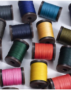 Flat lay of multiple colorful 0.4mm round waxed thread spools on white textured background