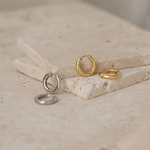Macro shot of minimalist gold and silver stainless steel hoop earrings on stone