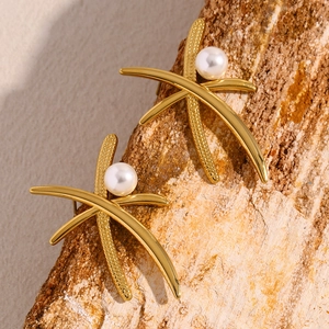 Macro shot of 18K gold plated palm leaf earrings with pearls on natural bark background