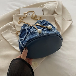 Chic blue denim bucket bag with gold chain strap and pearl accents shown in casual style